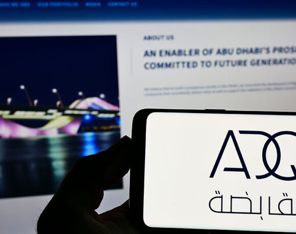 Close-up shot of a smartphone with the ADQ logo kept in front of an ADQ website on account of its investments in Tech Startups.