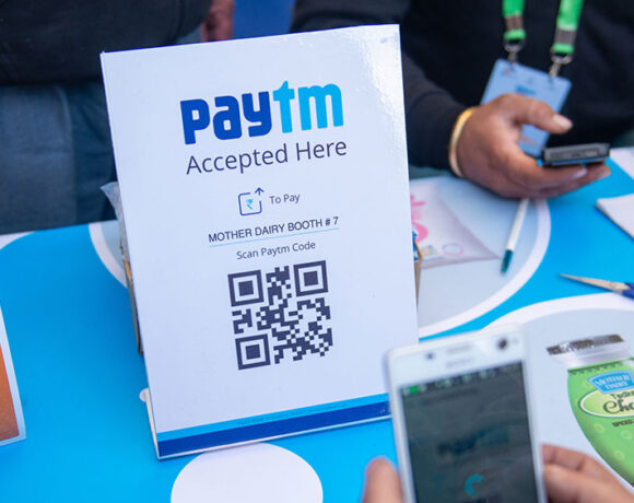 A person is holding a smartphone and prepared with a QR code scanner to digitally pay amount via PayTm.