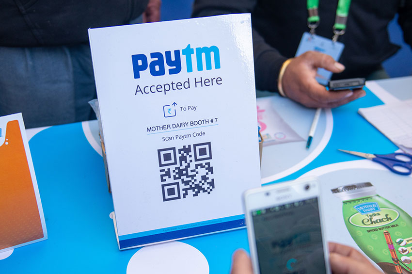 A person is holding a smartphone and prepared with a QR code scanner to digitally pay amount via PayTm.