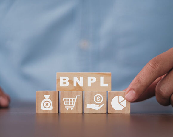 A person is holding a icons among four like cart, pie chart, dollars are kept on a table where a small wooden piece can be seen with letters BNPL