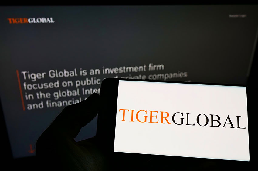 Closeup shot of a person holding a smartphone that has a logo of Tigerglobal in front of laptop that displays the core concept of TigerGlobal