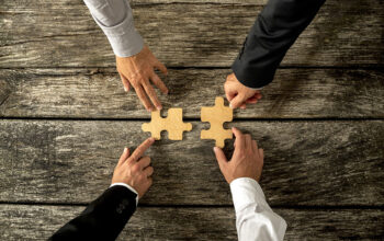Four successful business men joining two puzzle pieces each being held by two partners, depicting the concept of merger of two business companies.