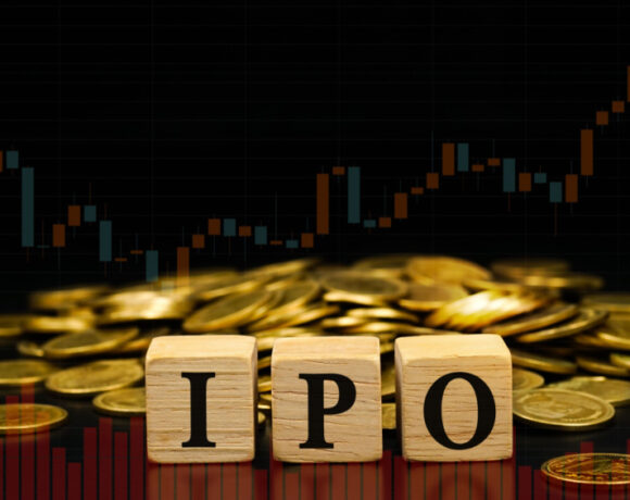 The initials IPO for Initial Public Offering are written on wooden blocks on a pile of gold coins with a graph on a black background.