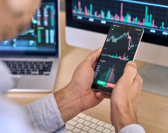 An over-shoulder view of a crypto investor using a smartphone app to analyze financial data, checking the stock market price, and checking the online trading platform.