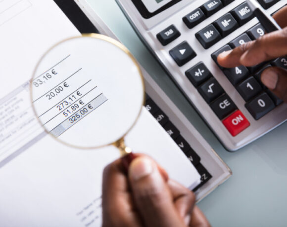 A close-up shot of a businessman holding a magnifying glass over an invoice illustrates the joint efforts of Sunlight and Finovox to fight against insurance fraud.